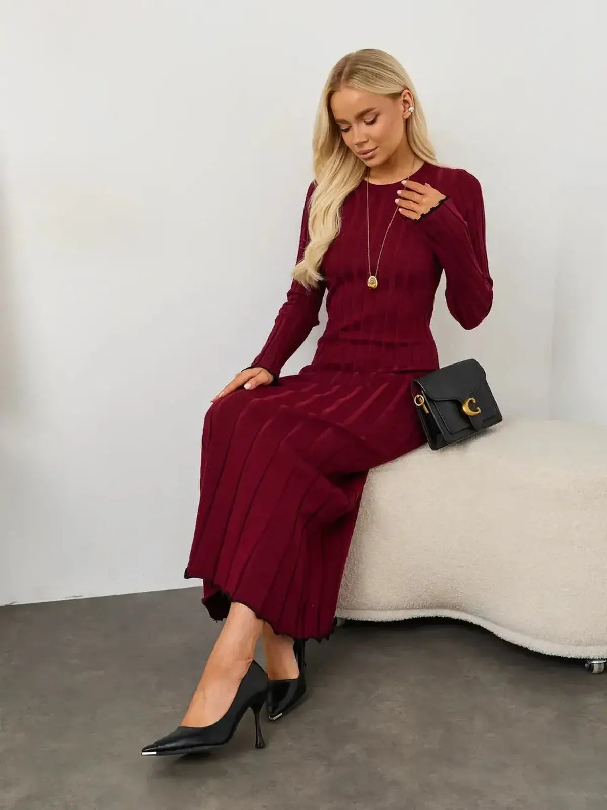 Burgundy midi dress with ribbed knit, elegant slim fit, styled with high heels and a small handbag.