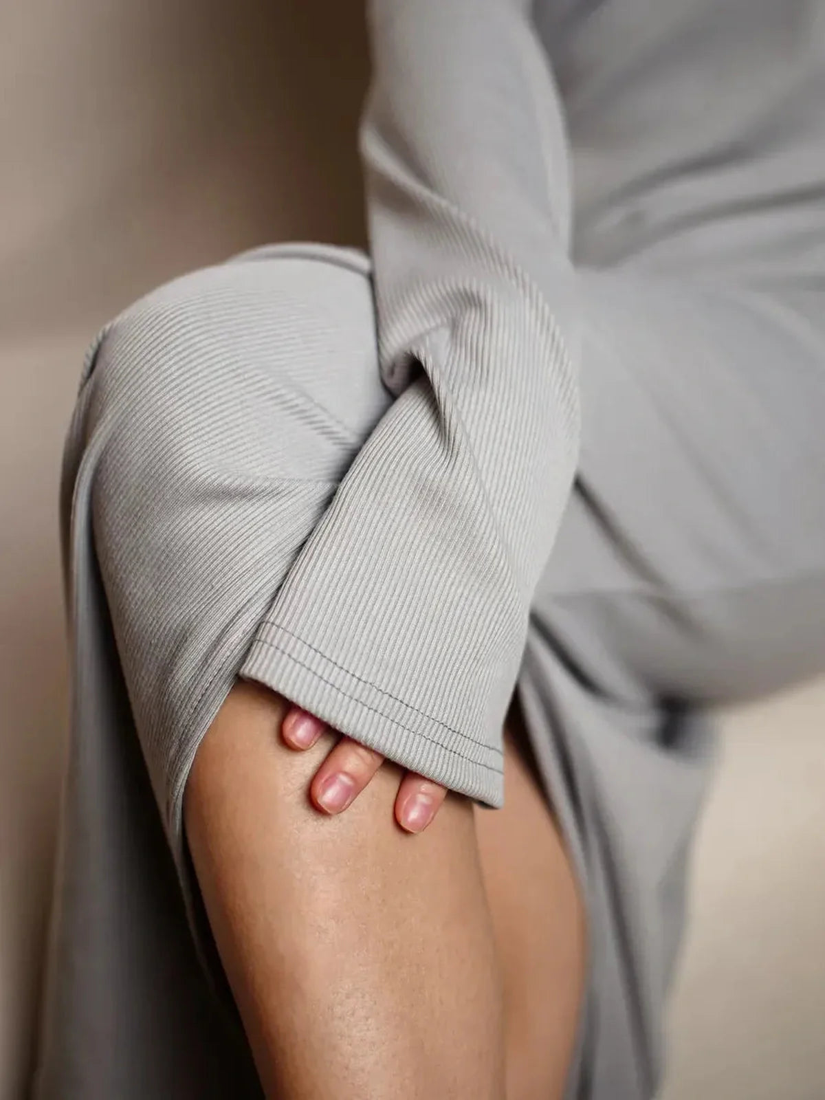 Close-up of a woman in a light grey maxi dress, showcasing the soft ribbed texture and elegant off-shoulder design.