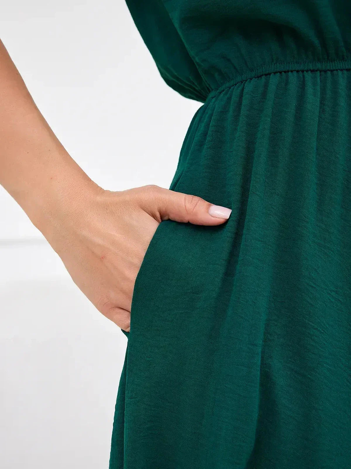 Close-up of a hand reaching into the pocket of the Emerald Aura Maxi Dress in lush green, showcasing its elegant design.