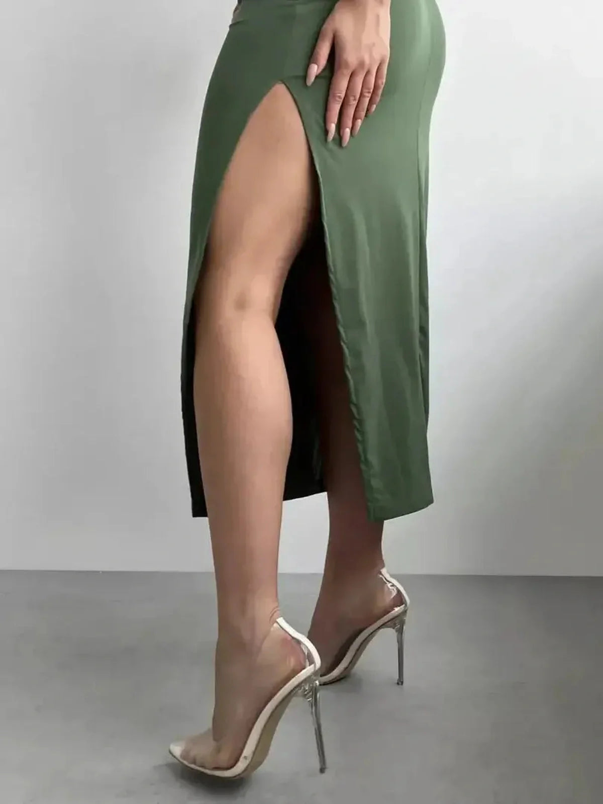 Side view of a woman wearing the Verde Curve Midi Dress with a thigh-high slit paired with clear heels.