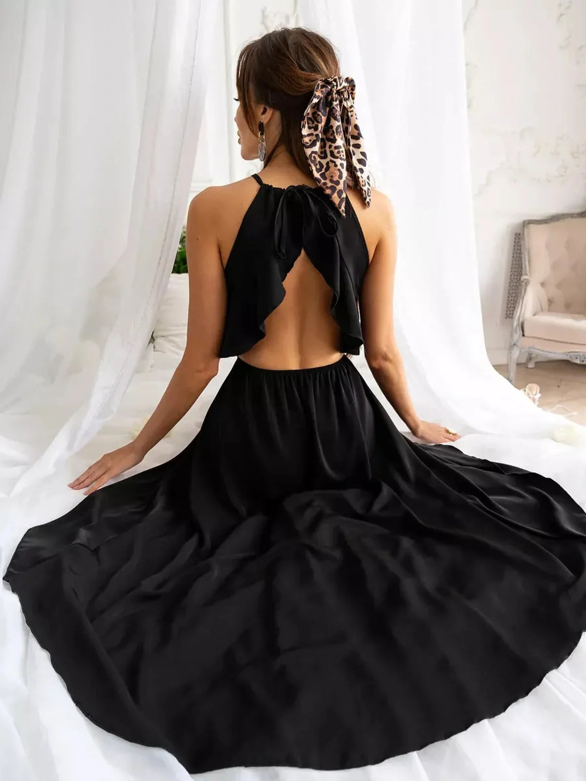 Elegant black midi dress with open back and halter neckline, perfect for summer evenings or wedding guest attire.