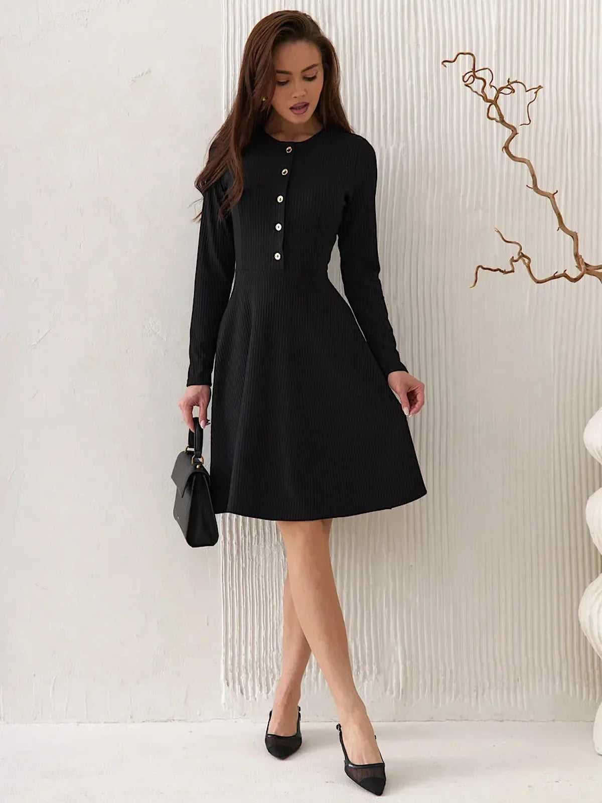 Model wearing a stylish Mod Noir black mini dress with long sleeves and button detail, perfect for formal and casual occasions.
