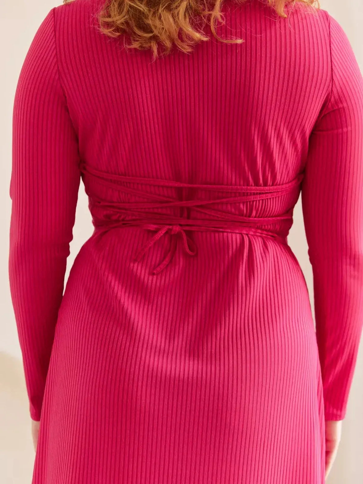 Back view of a woman wearing a pink contour midi dress with waist-tie detailing, showcasing its elegant ribbed design.