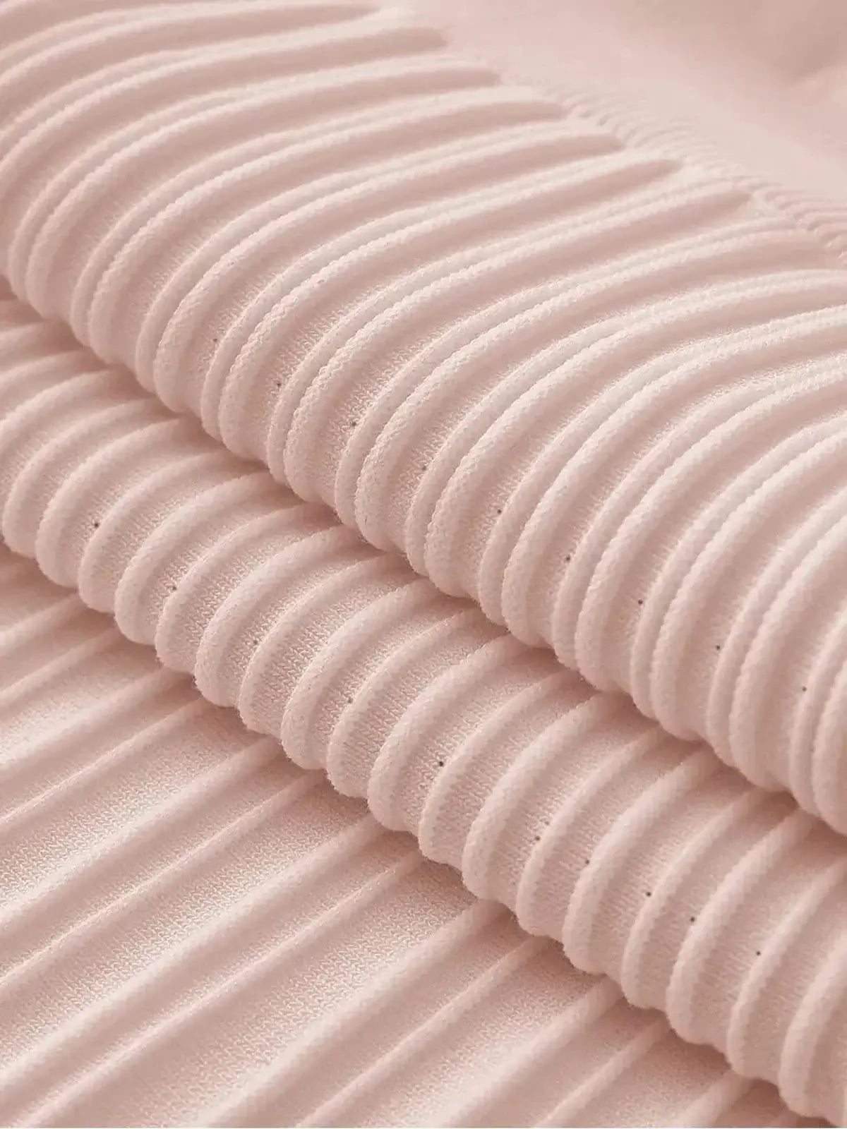 Close-up of luxurious ribbed knit fabric in soft blush color, showcasing texture for elegant dresses.