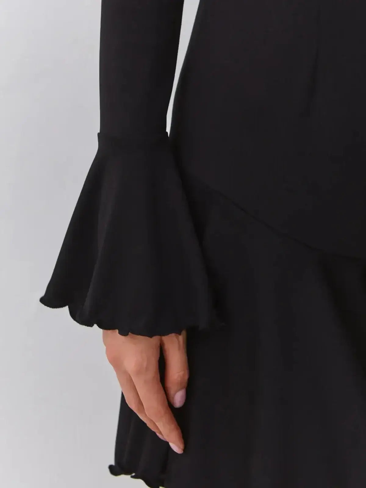 Close-up of a black dress with bell sleeves and flowing hem, highlighting elegant details in the fabric.