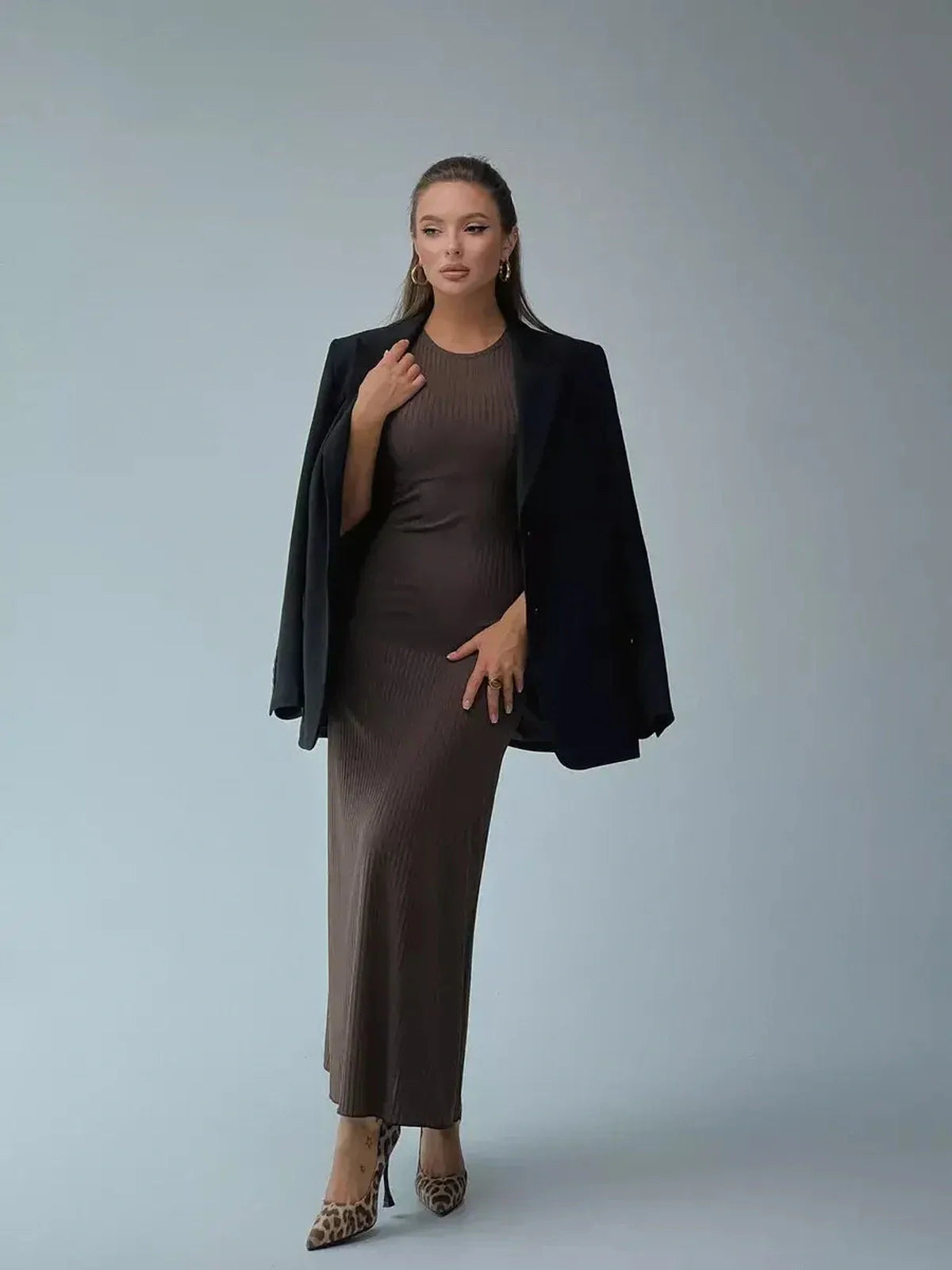 Model showcasing the Maxi Dress Sculpted Ease, a sleek ribbed knit dress, paired with a black blazer for an elegant look.