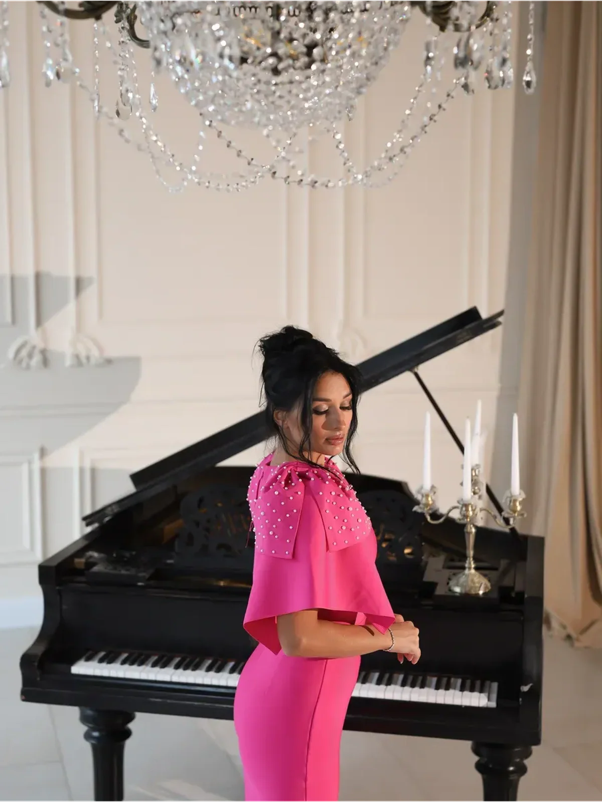 Model showcasing the Pearl Cape Midi Dress in fuchsia, featuring pearl embellishments, against an elegant piano backdrop.