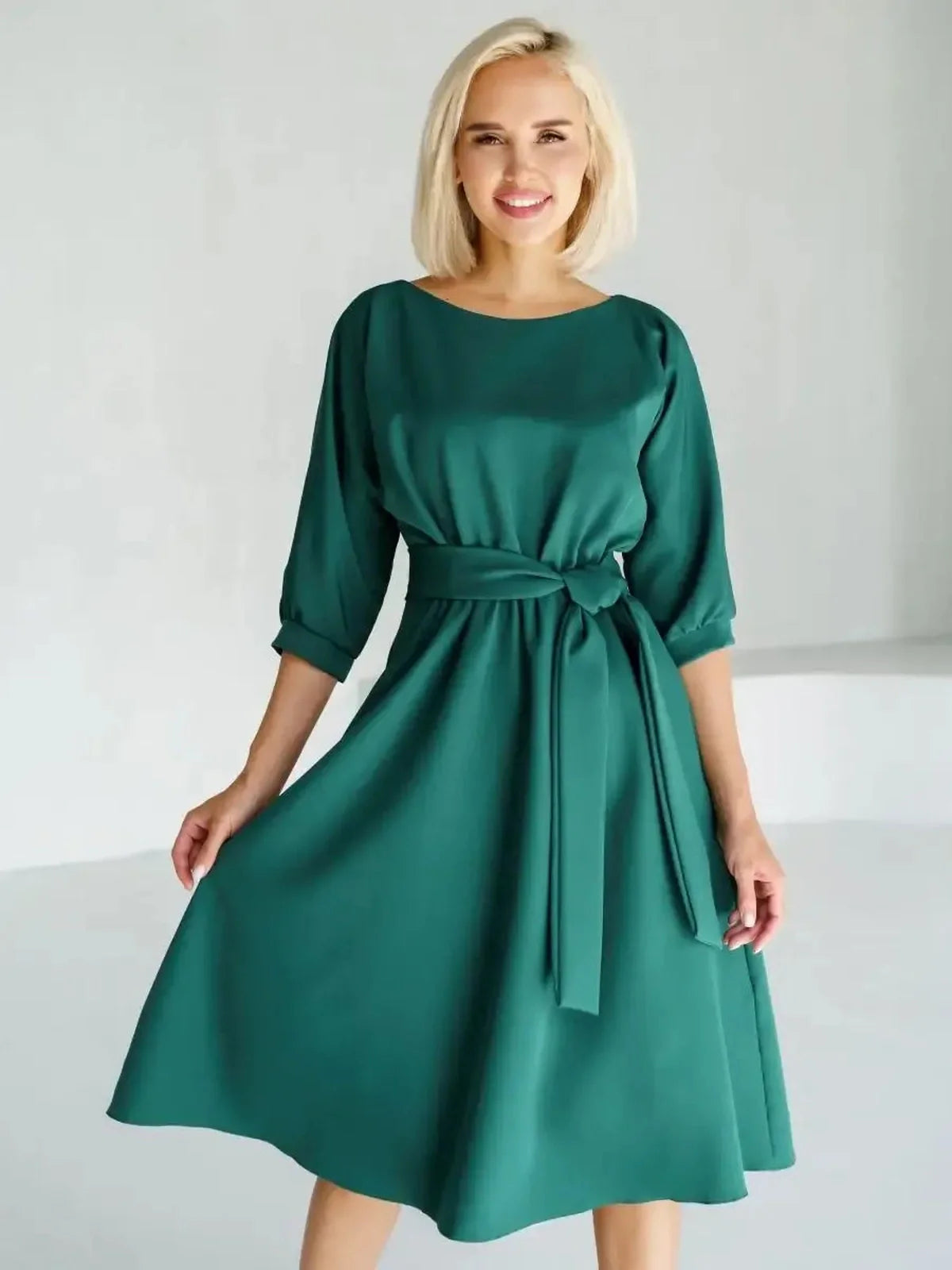 Elegant woman in an emerald green midi dress with a belt and A-line silhouette perfect for summer or wedding guest occasions.