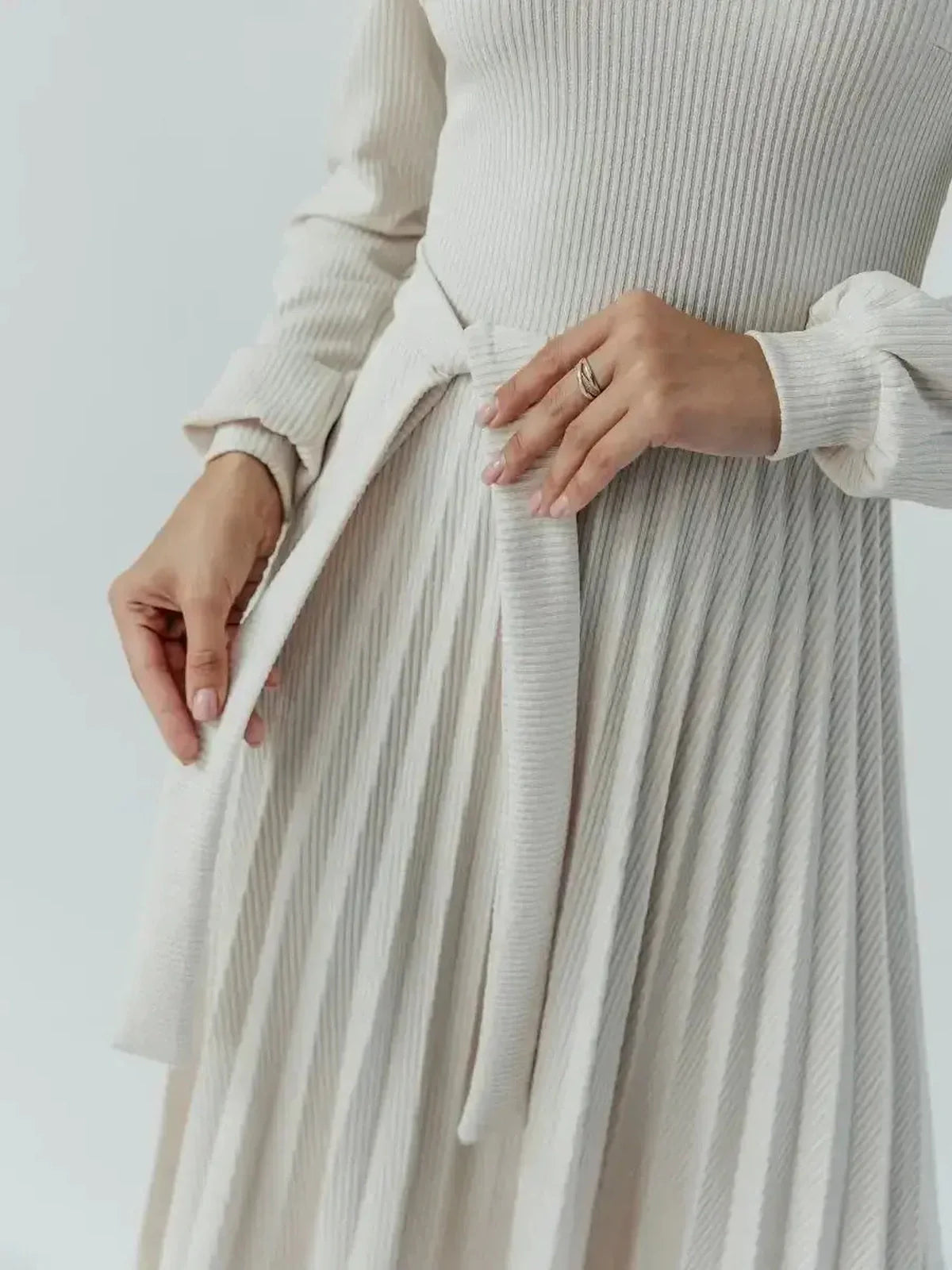 Close-up of a woman tying the belt of a Grace Pleat Midi Dress, showcasing its elegant knit and pleated skirt design.