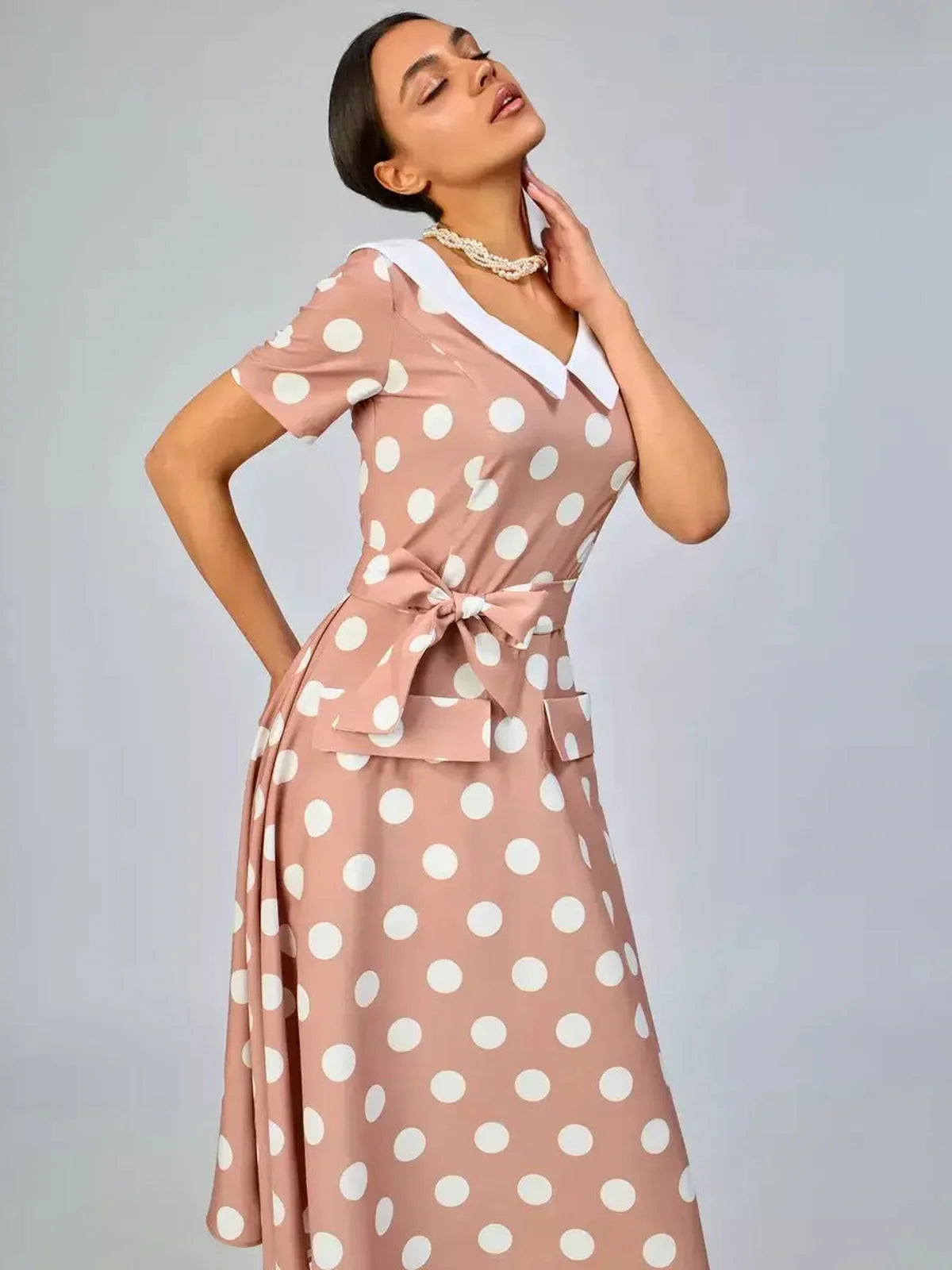 Vintage Muse Midi Dress in pink polka dots with a white collar and bow detail, perfect for summer parties and weddings.