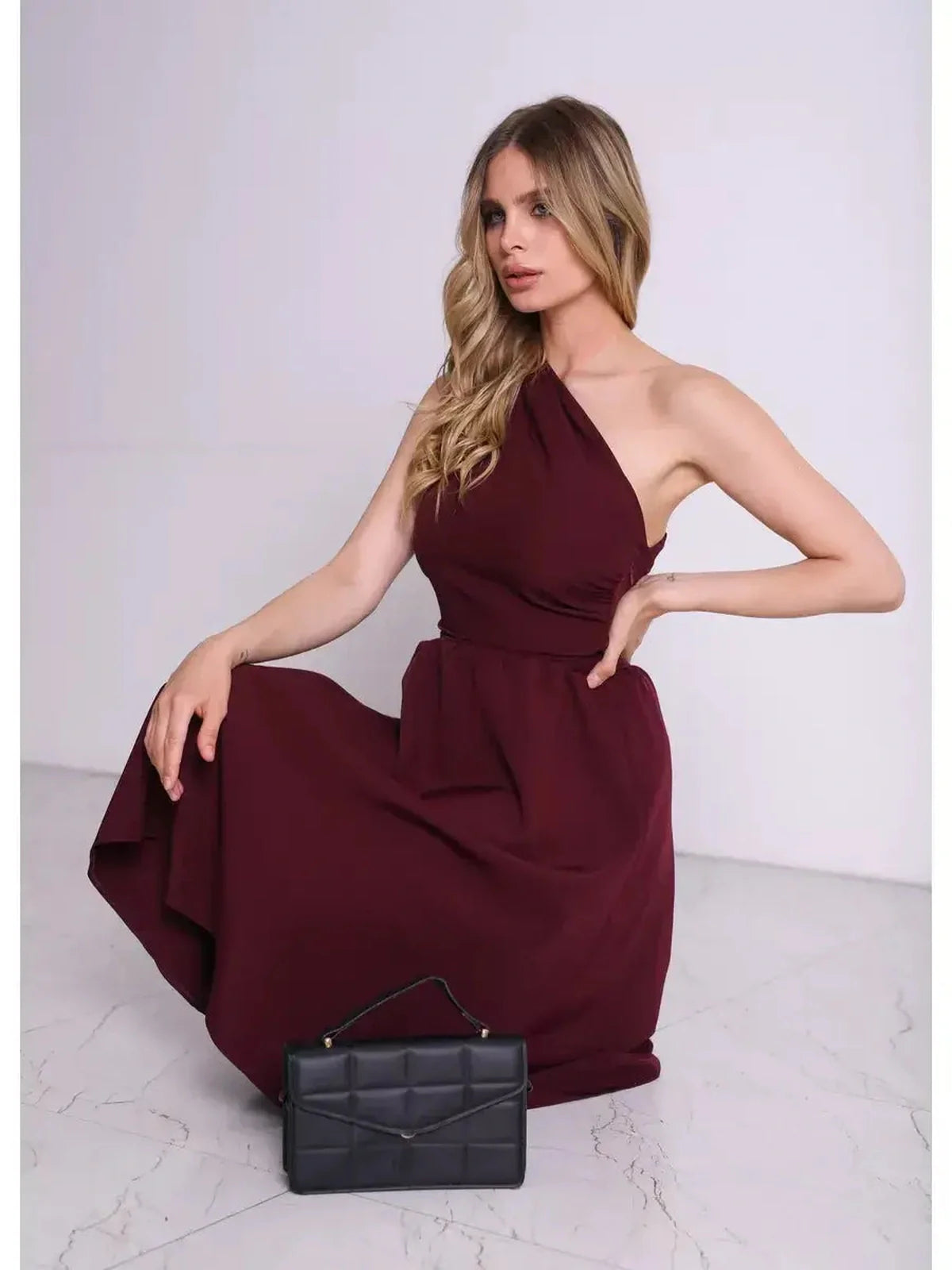 Model wearing a burgundy Opéra Midi Dress featuring a one-shoulder design, paired with a stylish black handbag.