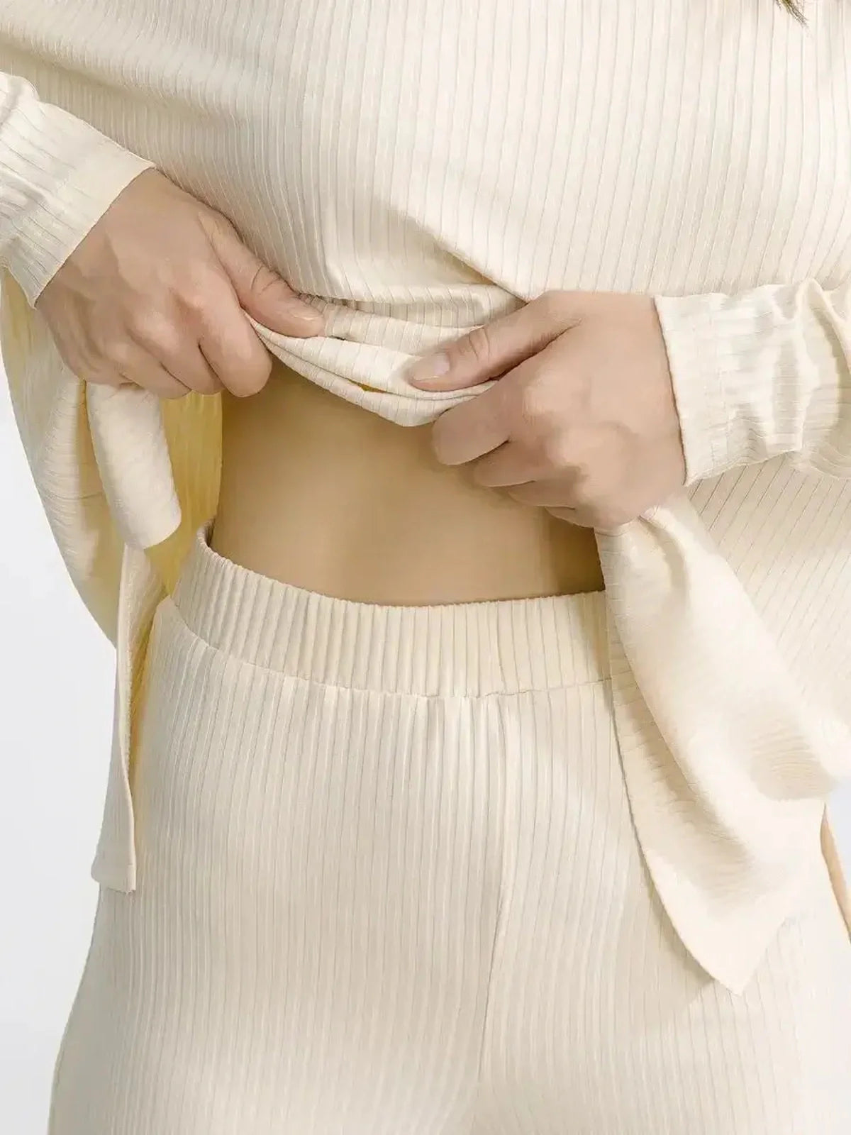 Close-up of a person adjusting the hem of an oversized beige soft ribbed two-piece lounge set.