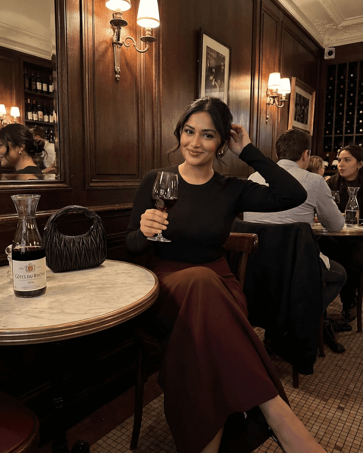 Woman wearing Merlot Maxi Skirt, holding a glass of wine in an elegant restaurant setting.