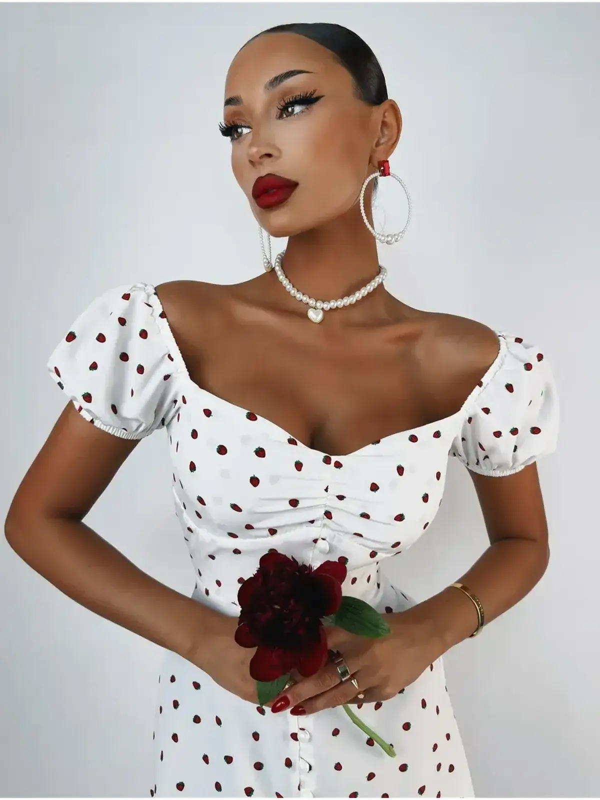 Model in a white polka dot Luxe Charm Mini Dress, holding a flower, showcasing a chic wedding guest outfit.