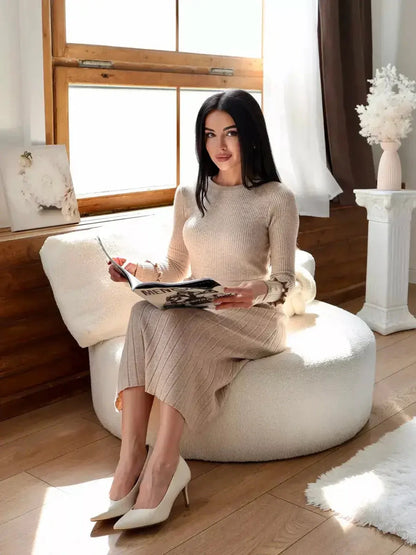 Woman in a ribbed knit midi dress sits elegantly, holding a magazine in a bright, cozy indoor setting.