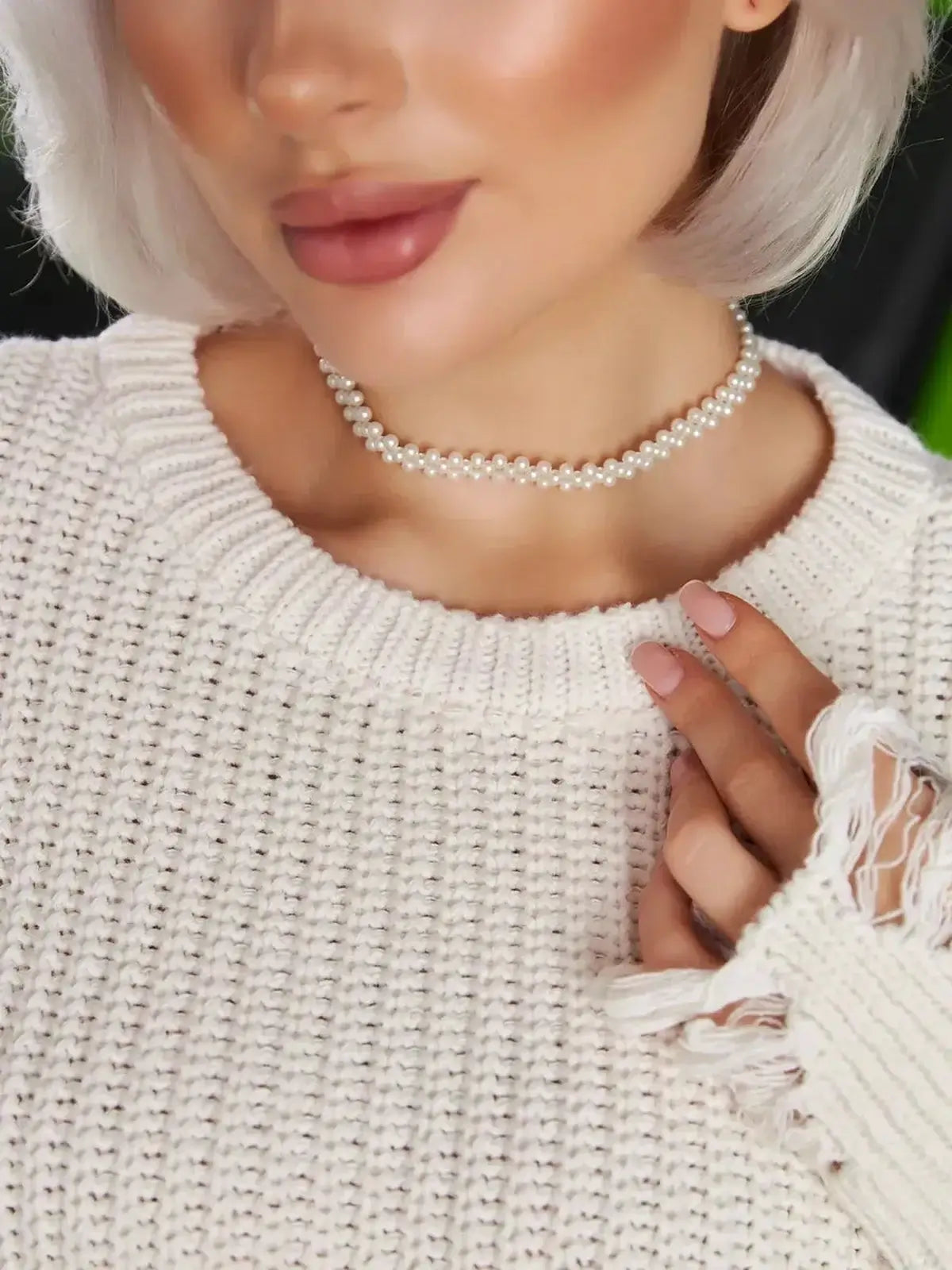 Model wearing a cozy white sweater with distressed sleeves and a pearl choker, showcasing a chic, relaxed style.