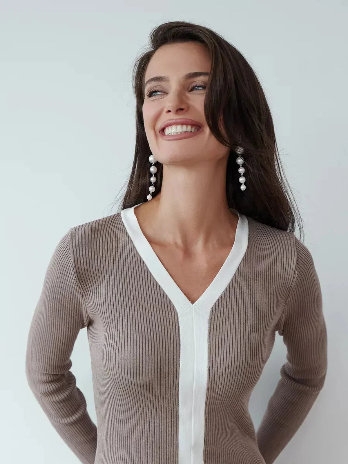 Smiling woman in a cappuccino-toned ribbed knit dress with white V-neckline, showcasing modern elegance.