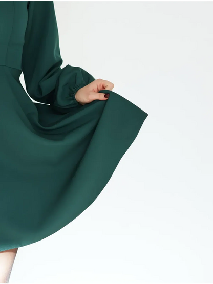 A close-up of a woman's hand holding the skirt of a green mini dress, showcasing its elegant silhouette.