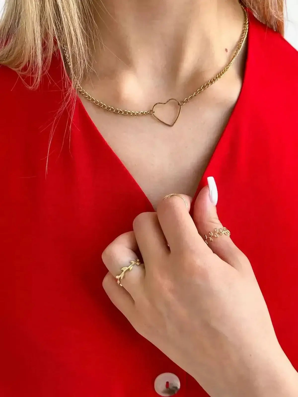 Close-up of a woman wearing a heart-shaped gold necklace with rings against a crimson dress, showcasing stylish accessories.