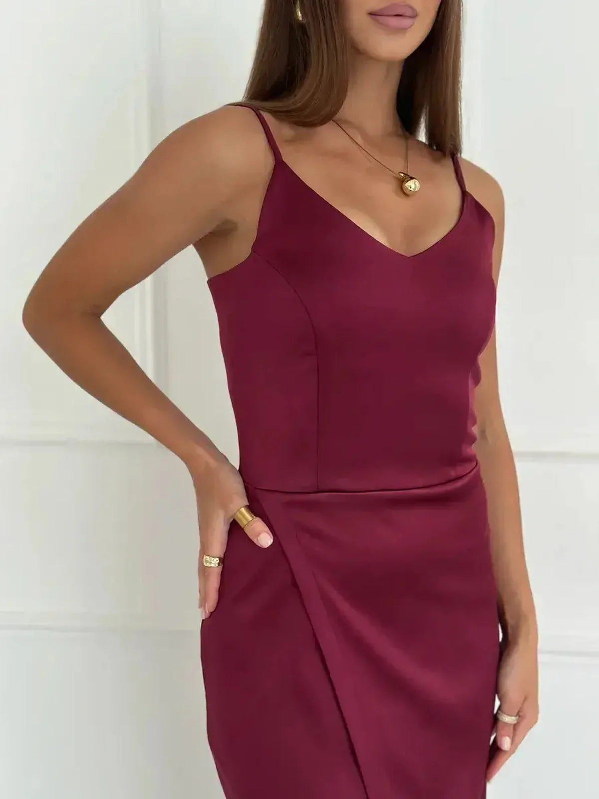 Close-up of a woman wearing a burgundy satin midi dress with a wrap detail and adjustable straps, showcasing elegance.