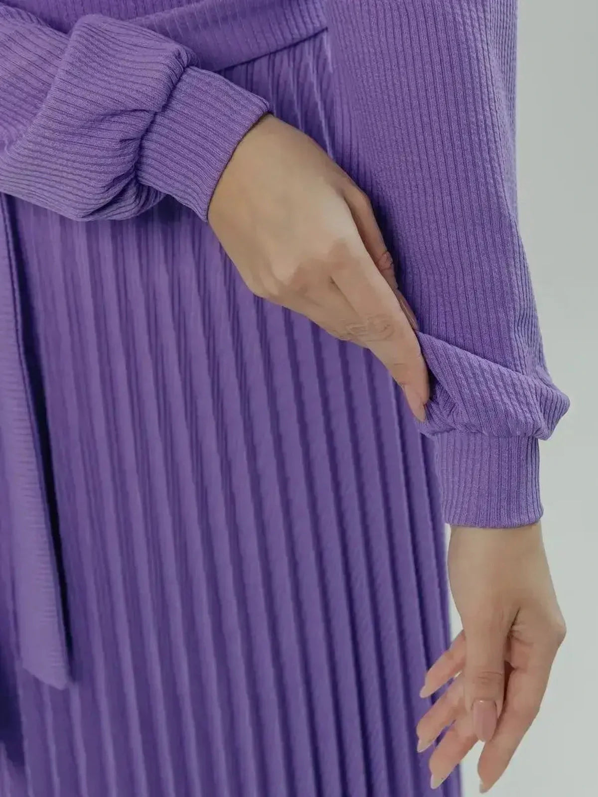 Close-up of woman's hand adjusting sleeve of Serena Midi Dress, showcasing pleated violet fabric and elegant style.