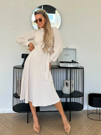 Model showcasing the Ivory Whisper Midi Dress with flowing pleated skirt and ribbed texture in a stylish setting.