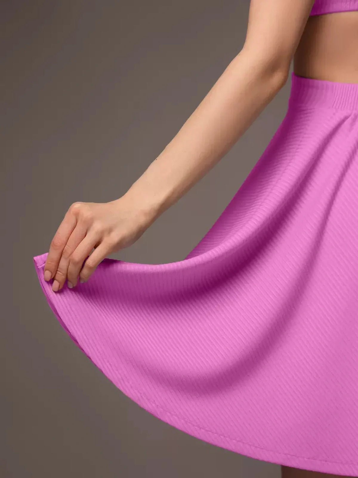 Close-up of a woman's hand holding the flared hem of a pink Cutout Charm Mini Dress, showcasing its ribbed texture.