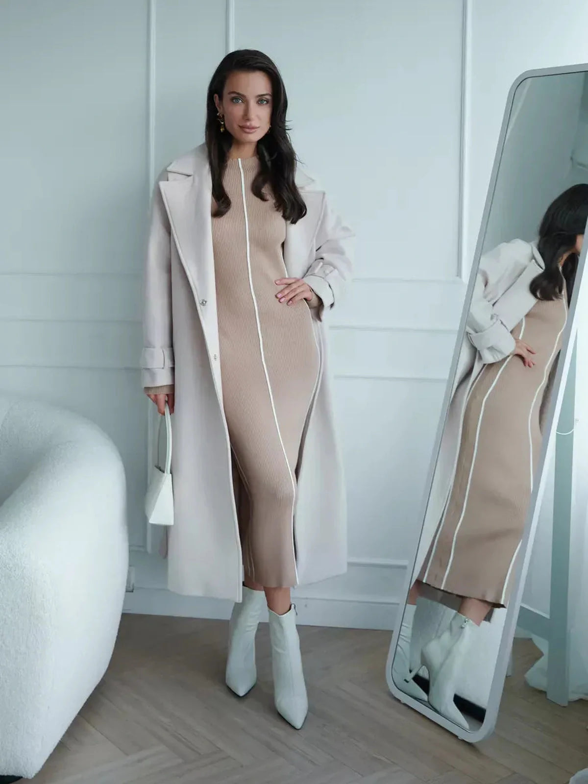 Model in a soft beige Sculpted Line Midi Dress paired with a light coat, showcasing elegant lines and a sophisticated look.