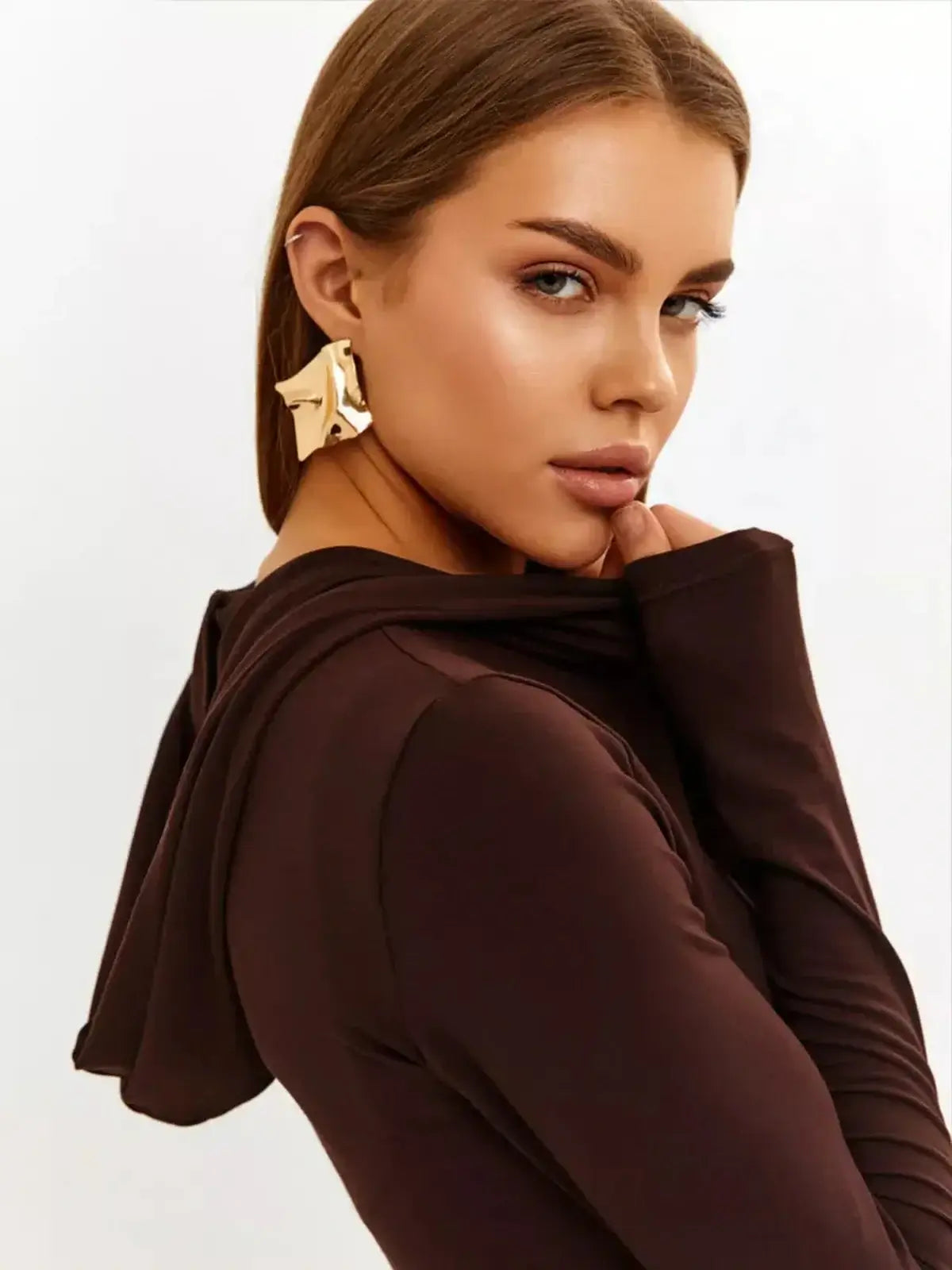 Close-up of a woman wearing a hooded brown dress, showcasing elegance and modern style with statement earrings.