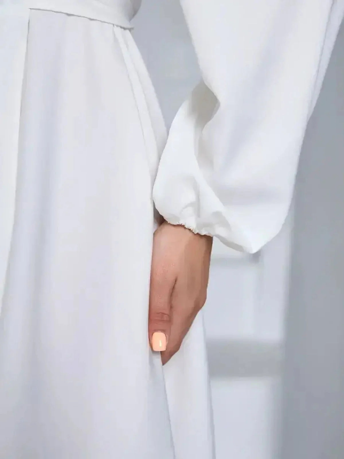 Close-up of a woman's hand on an ivory dress, showcasing the elegant fabric and design details of the long sleeve silhouette.