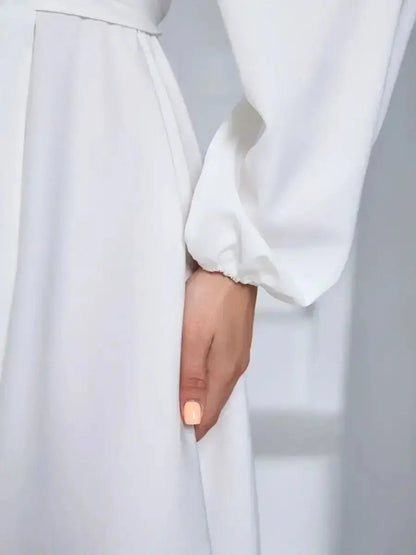 Close-up of a woman's hand on an ivory dress, showcasing the elegant fabric and design details of the long sleeve silhouette.