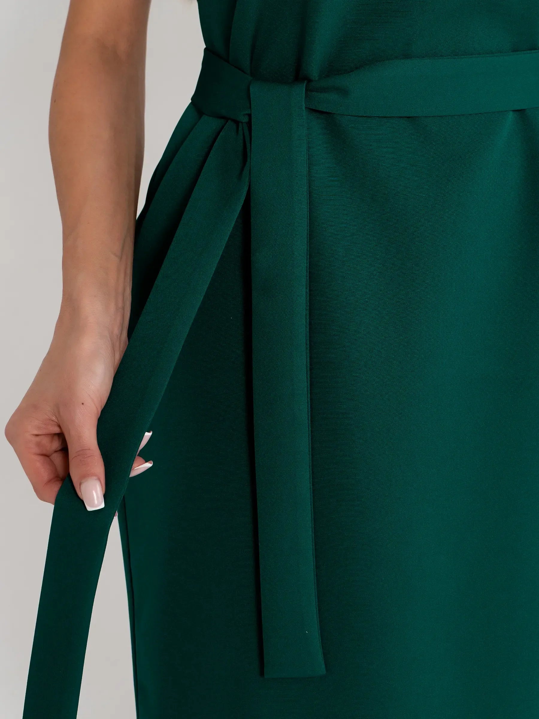 Close-up of a woman adjusting the fabric belt of a luxurious emerald green mini dress, showcasing elegance.