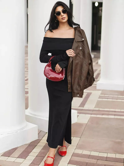 Model wearing an off-shoulder black maxi dress with a side slit, paired with a brown jacket and red accessories.