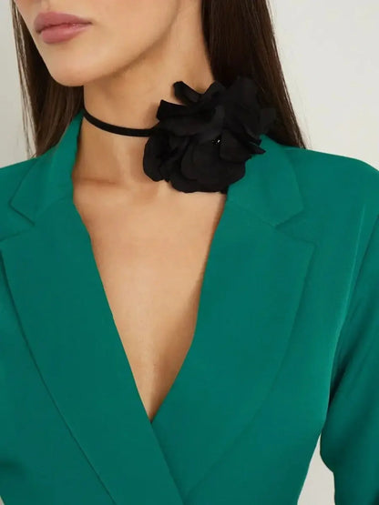 Close-up of a woman in an emerald green midi dress featuring a black flower choker, highlighting tailored elegance.