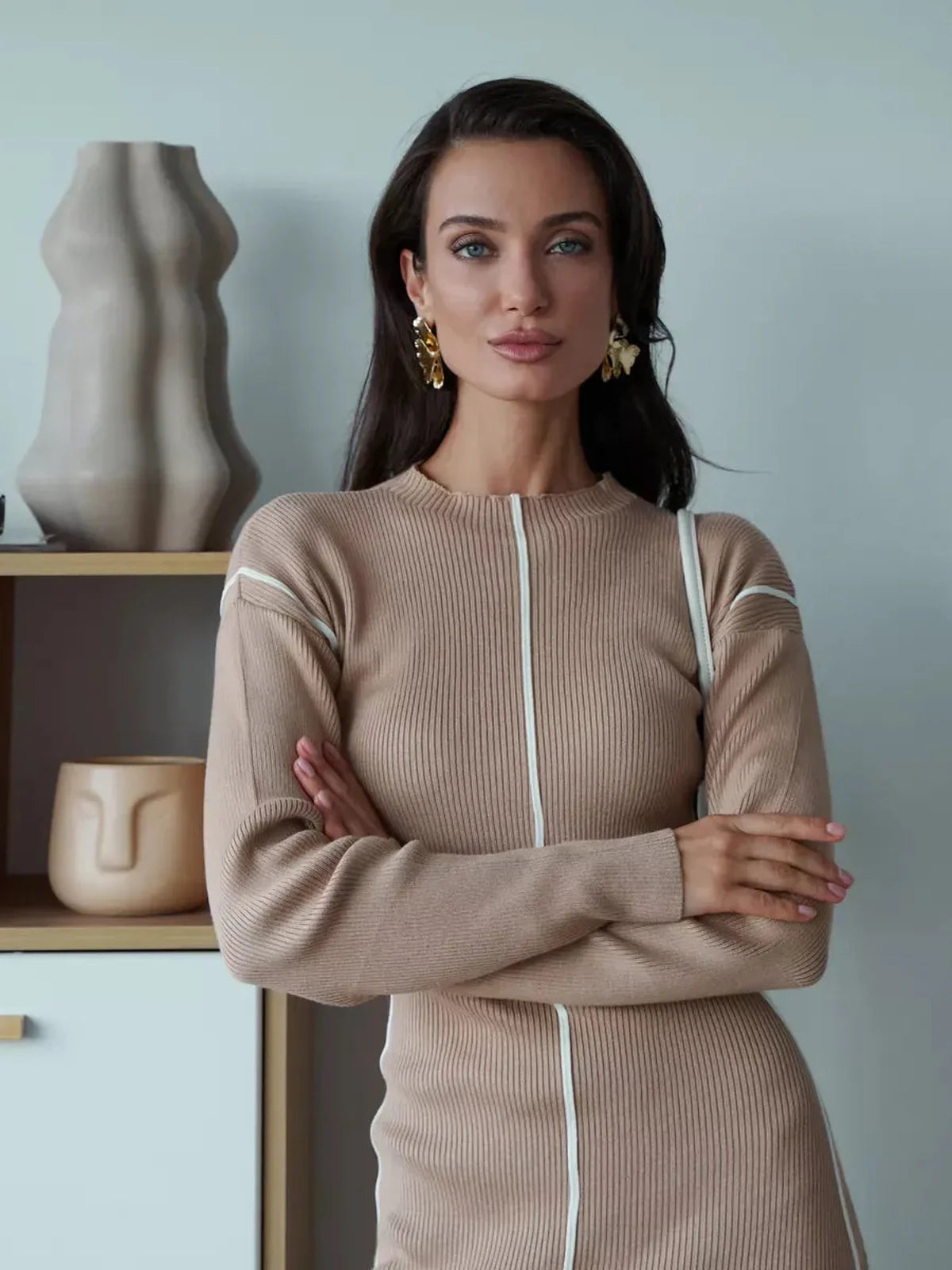 Model wearing a beige sculpted line midi dress with elegant silhouette and minimalist design in a chic indoor setting.