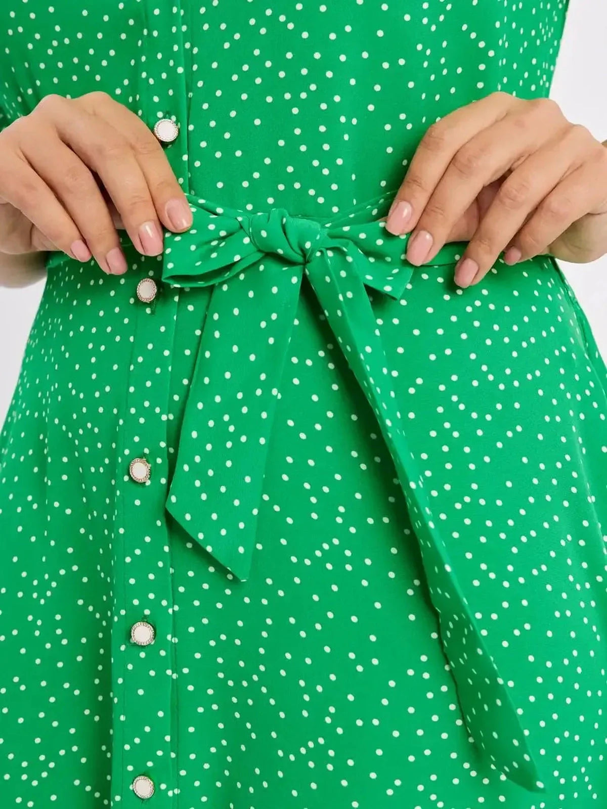 Close-up of a green midi dress with white polka dots, featuring a button-down front and a tied waist.