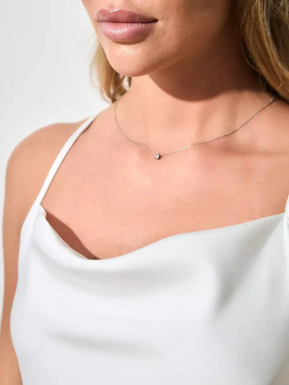 Close-up of a woman wearing a white satin dress with a delicate necklace, showcasing elegance and style.