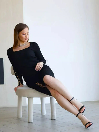 Model showcasing the Laced Allure Midi Dress with lace-up accents, sitting on a chair in a minimalistic setting.