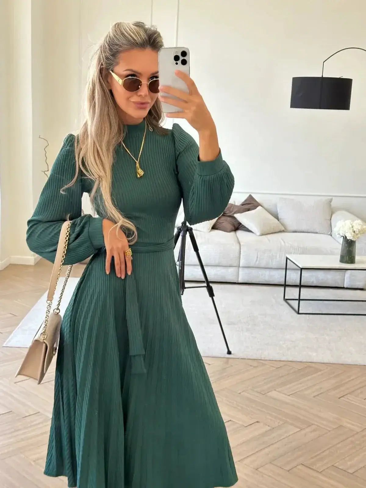 Elegant woman in an emerald ribbed midi dress, showcasing pleated design and stylish accessories in a chic setting.