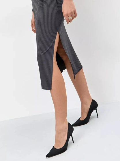 Close-up of a woman's leg in a ribbed knit midi dress with side slit, paired with elegant black heels.