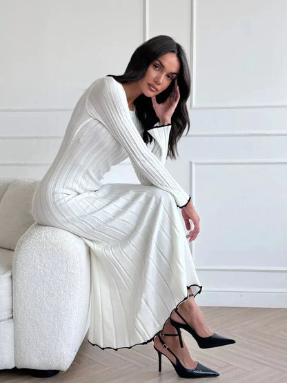 Ivory Grace Maxi Dress featuring sculpted ribbed knit silhouette and ruffle trim, styled with elegant black heels.