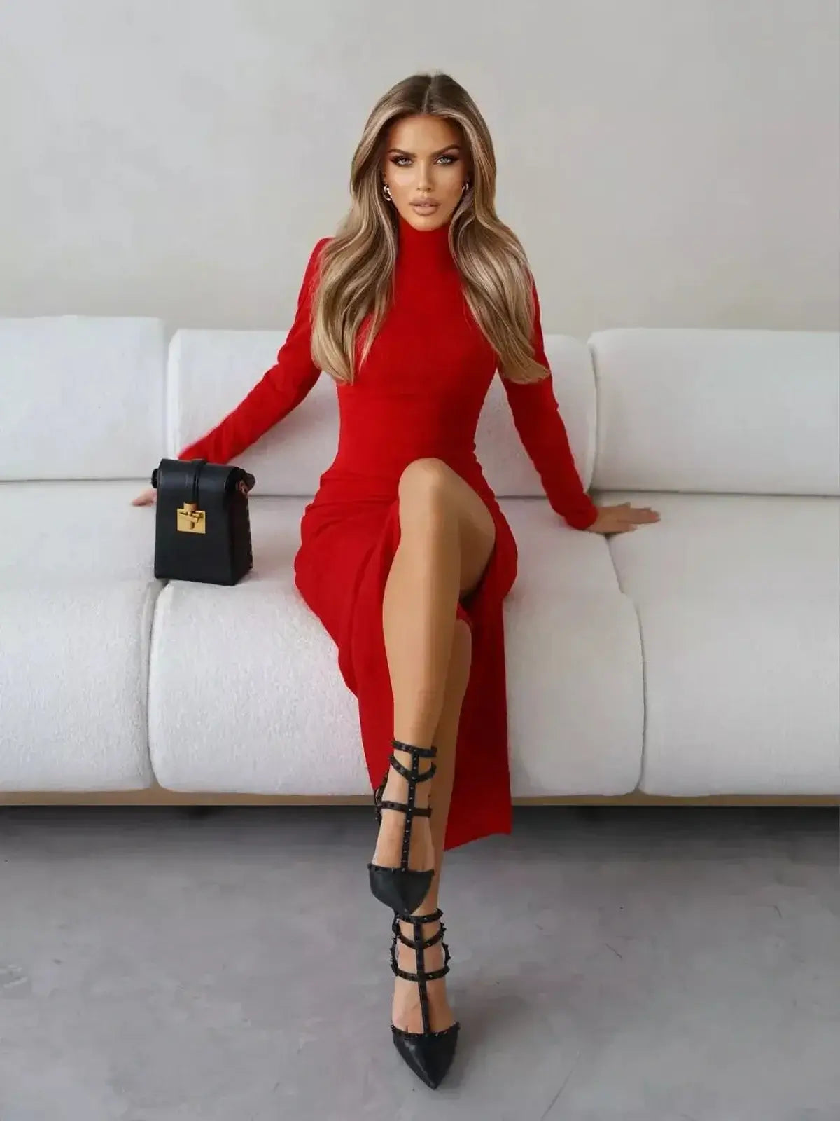 Sculpted red midi dress with long sleeves and a thigh-high slit, styled with black heels and a chic handbag.