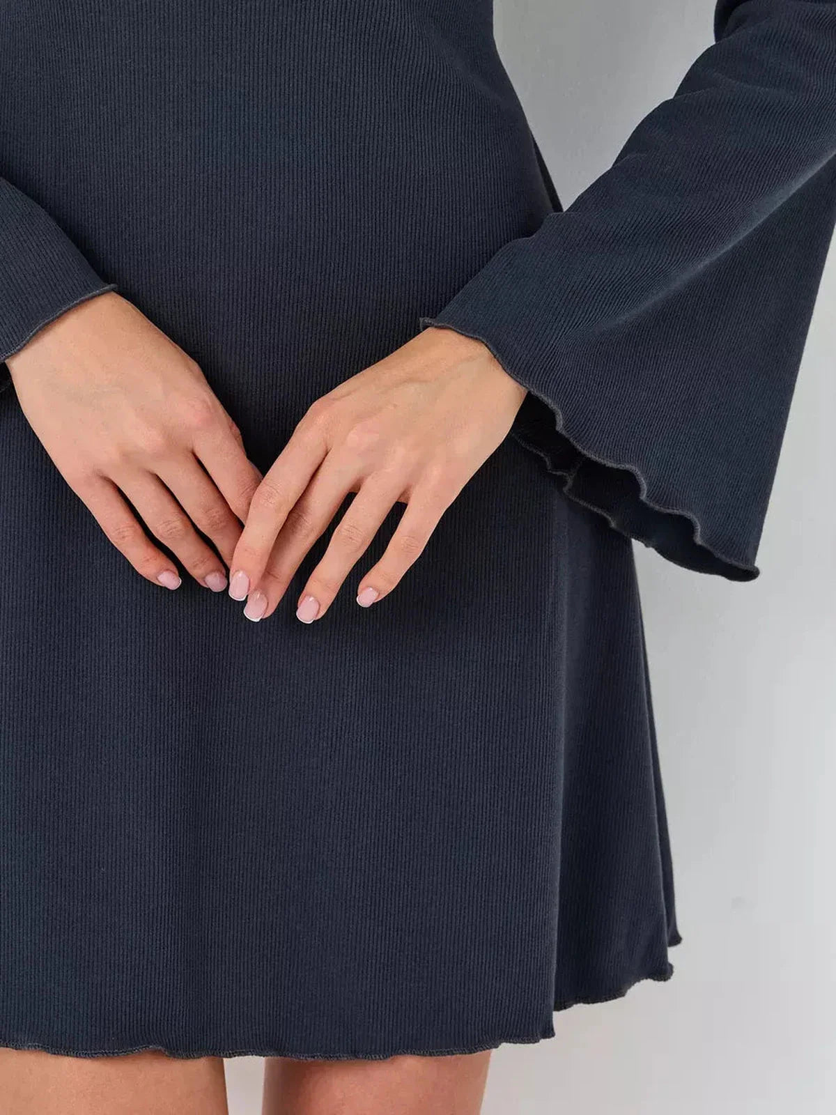 Close-up of hands on the Graphite Grace mini dress, highlighting its ribbed texture and flared sleeves.