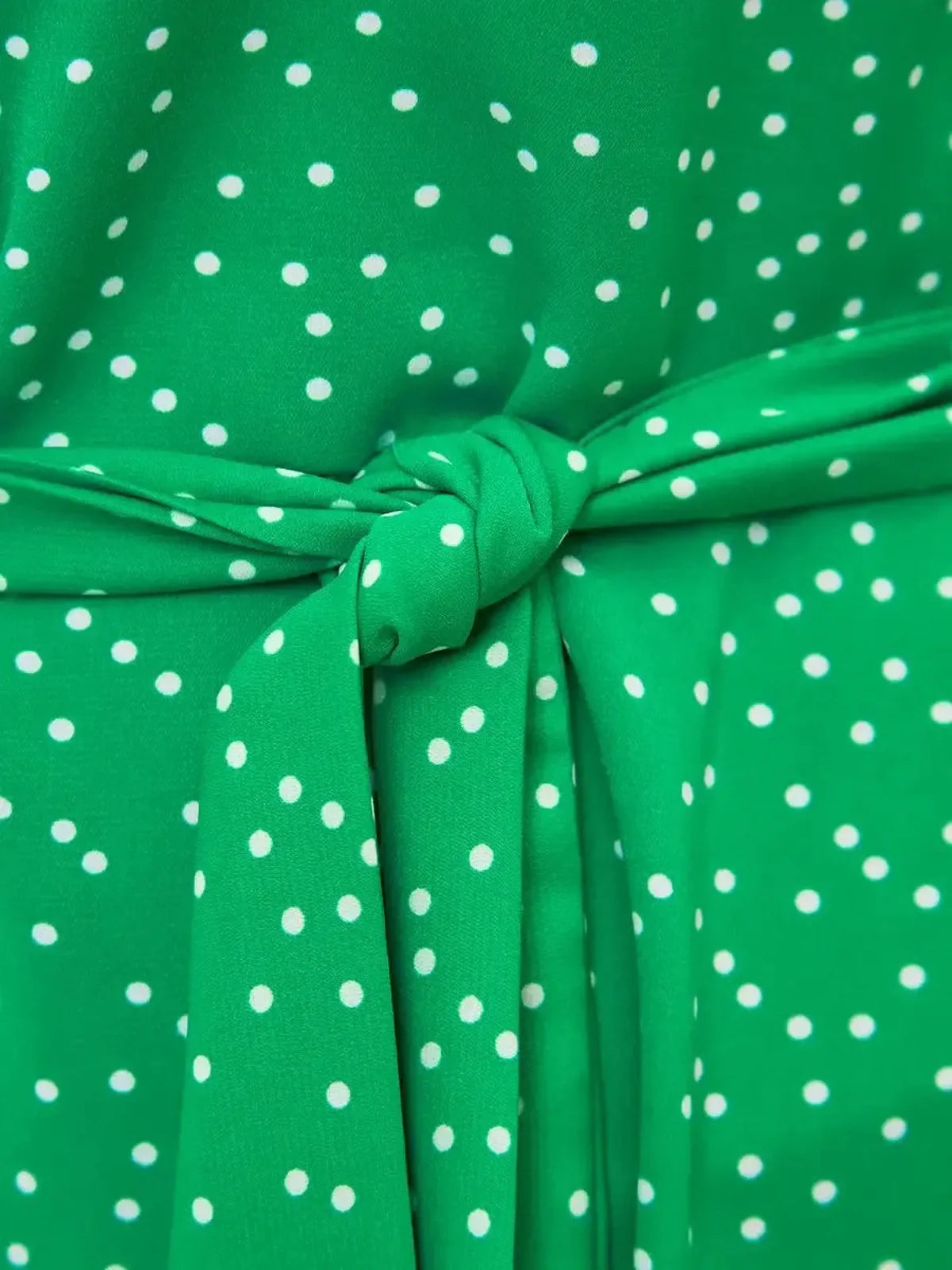 Close-up of a green midi dress with white polka dots and a tied waist detail, perfect for summer or wedding guest attire.