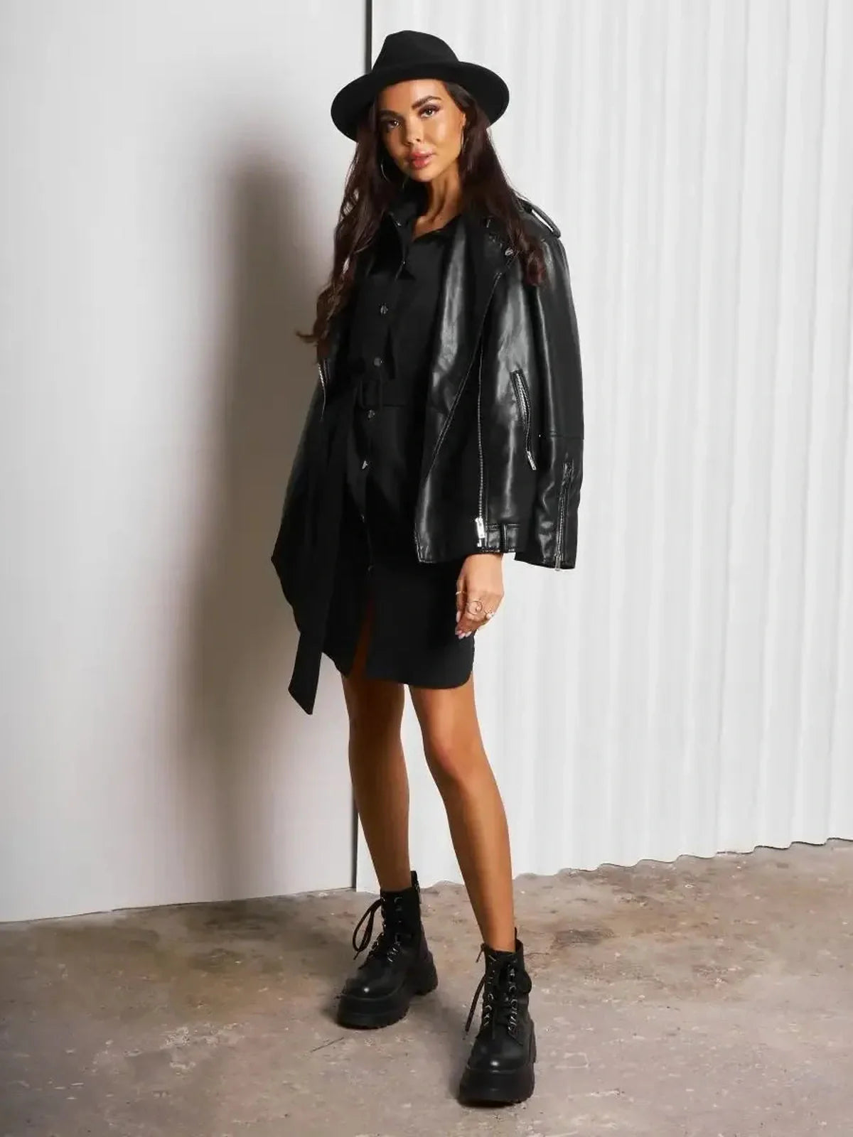 Model wearing an Urban Edit Mini black dress with a leather jacket and hat, showcasing a chic, edgy style.