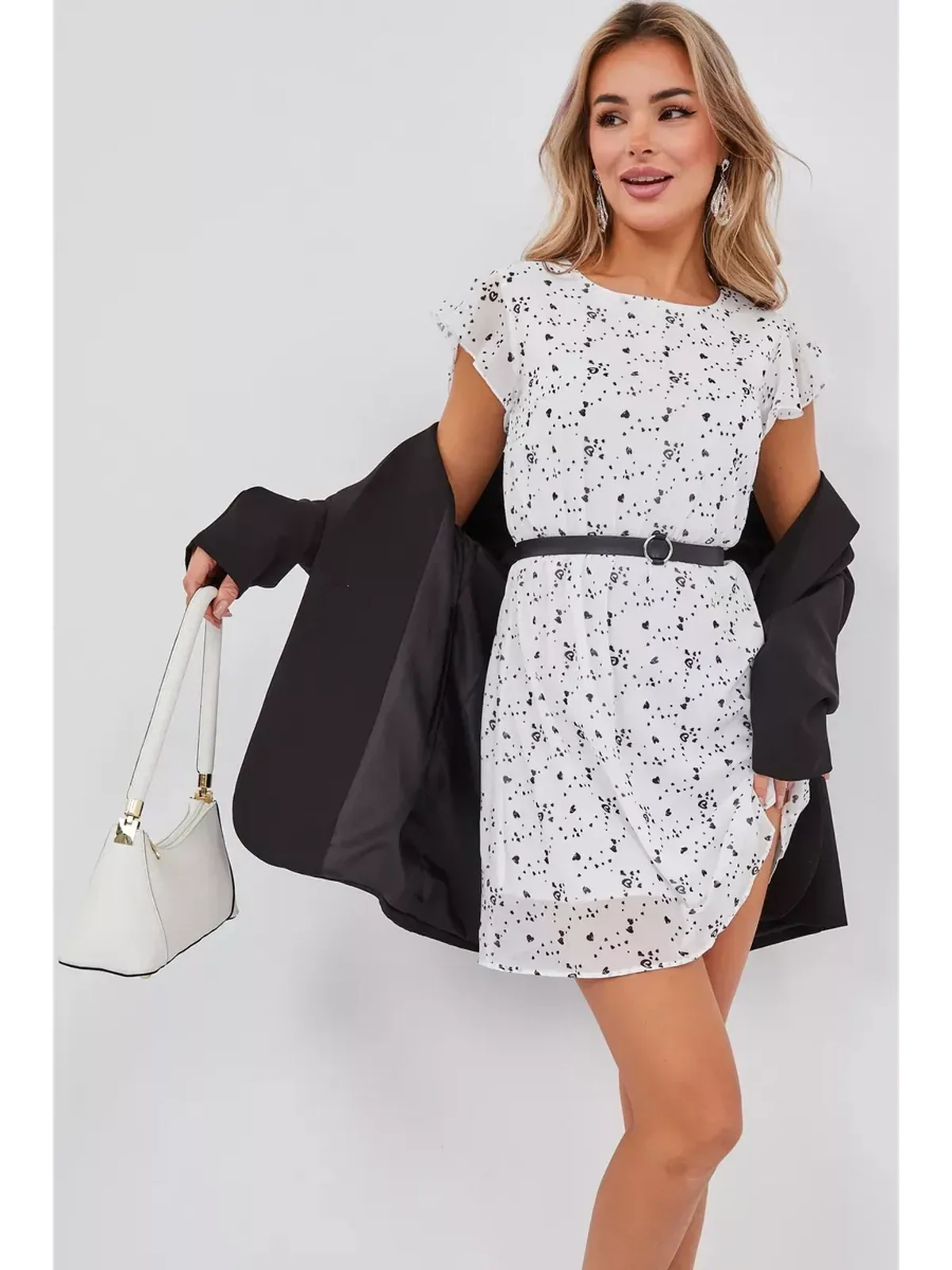 Woman wearing a Monochrome Muse Mini Dress with flutter sleeves and a black belt, paired with a stylish coat and handbag.