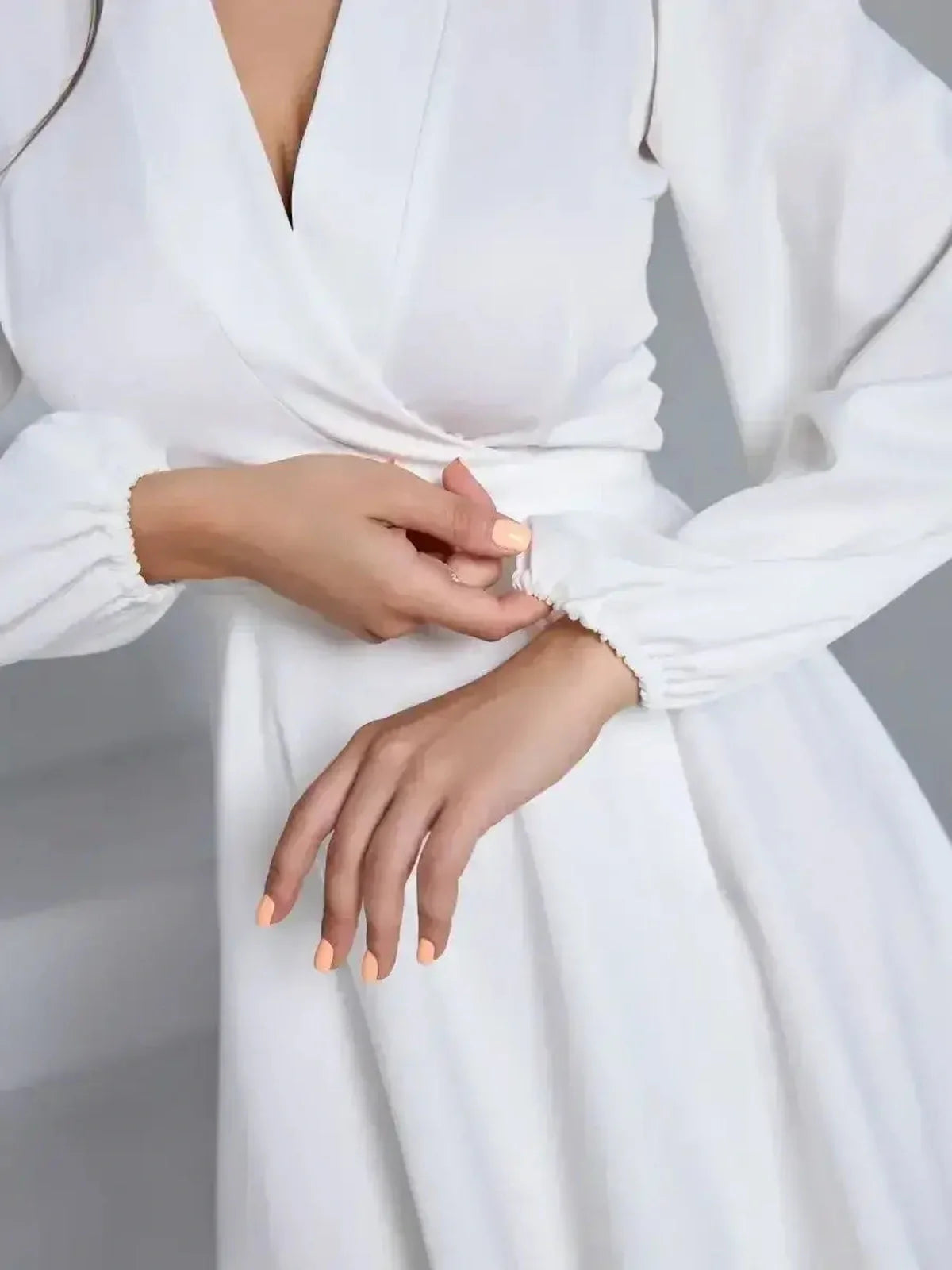 Close-up of a woman's hands adjusting the waist tie on an elegant ivory dress, showcasing its stylish design.