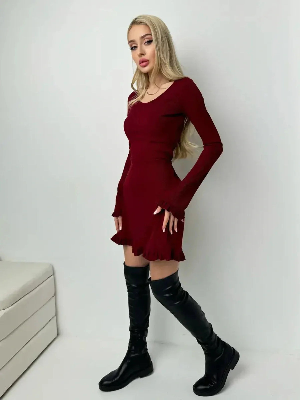 Model wearing a Crimson Flare ribbed mini dress with romantic ruffles and fitted silhouette, paired with knee-high black boots.