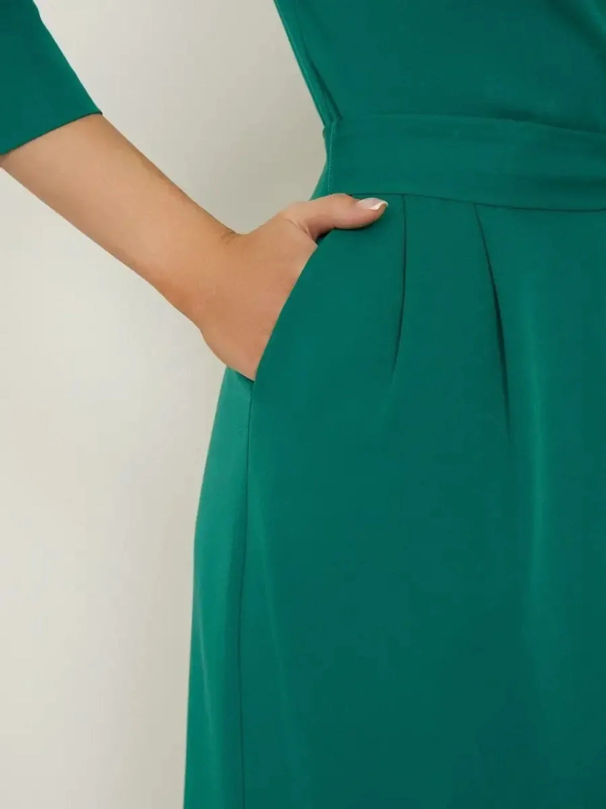 Close-up of the Sculpted Grace Midi Dress showcasing a hand in the pocket, highlighting its tailored elegance and emerald green fabric.