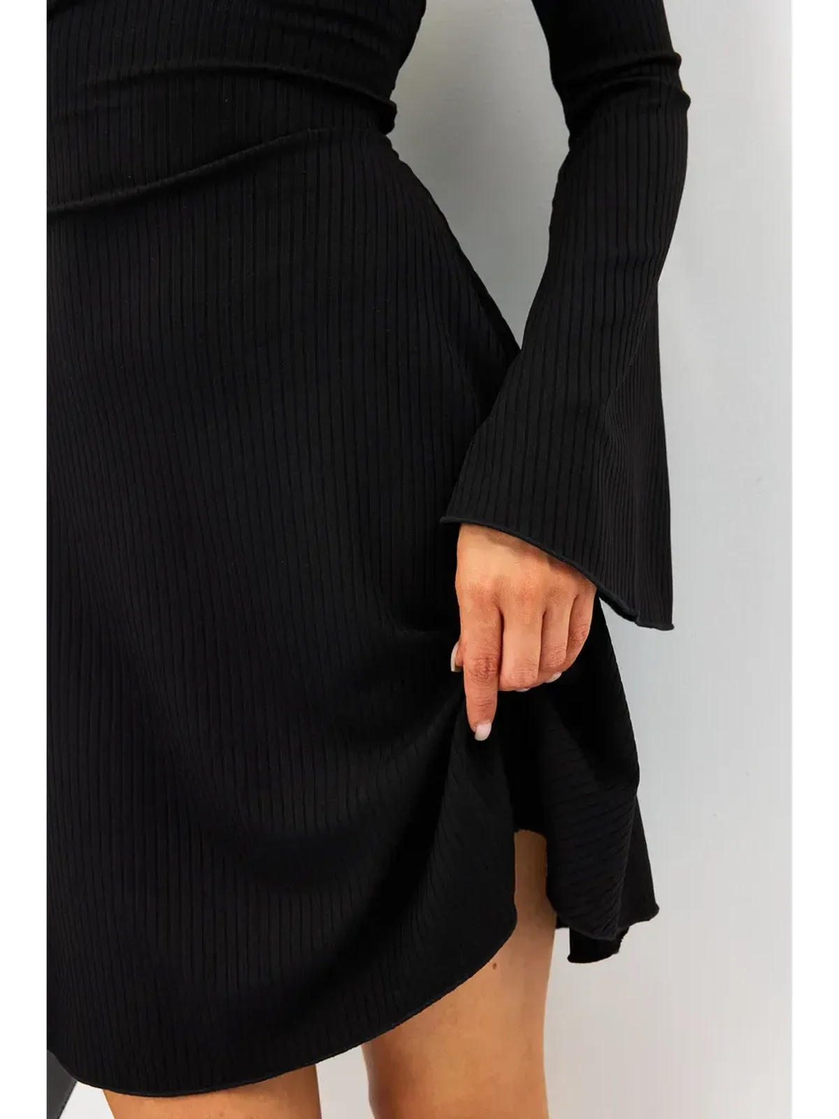 Close-up of a woman wearing a black ribbed Flare Charm Mini Dress with fluted sleeves and a playful silhouette.